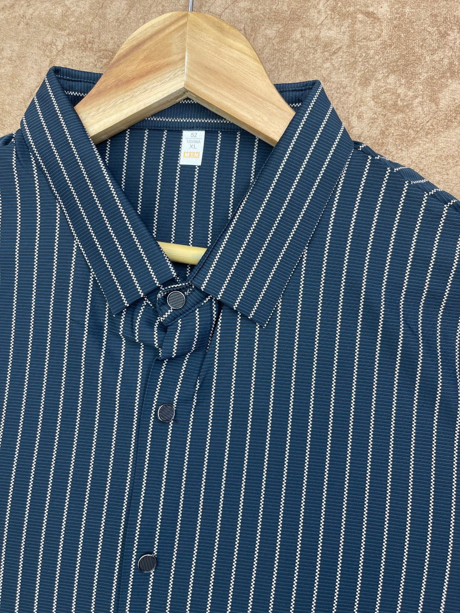 A close-up of a navy blue button-down shirt with thin white vertical pinstripes, hanging on a light wood hanger against a textured tan background.